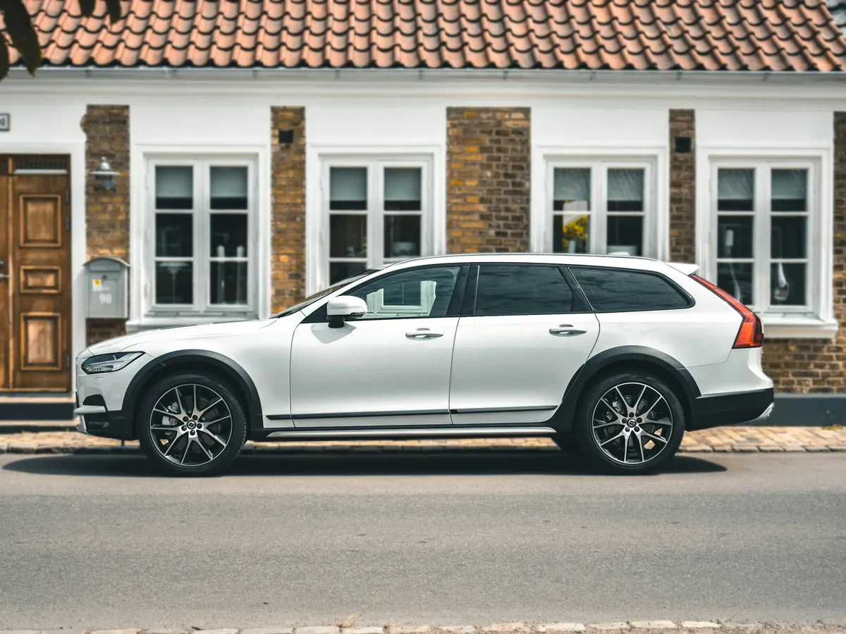 Białe Volvo kombi zaparkowane bokiem przed domem z cegły